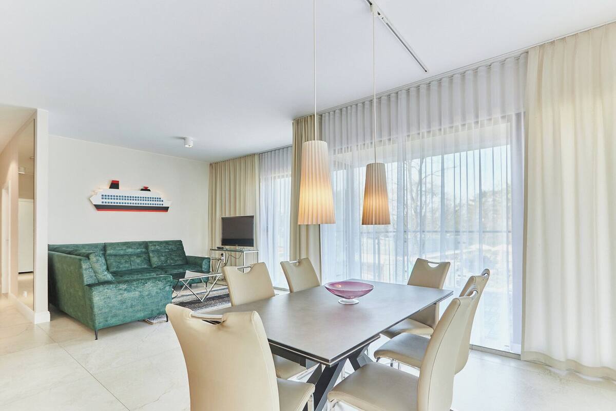 A modern hotel room with a dining area, a green sofa, and a large window with curtains.