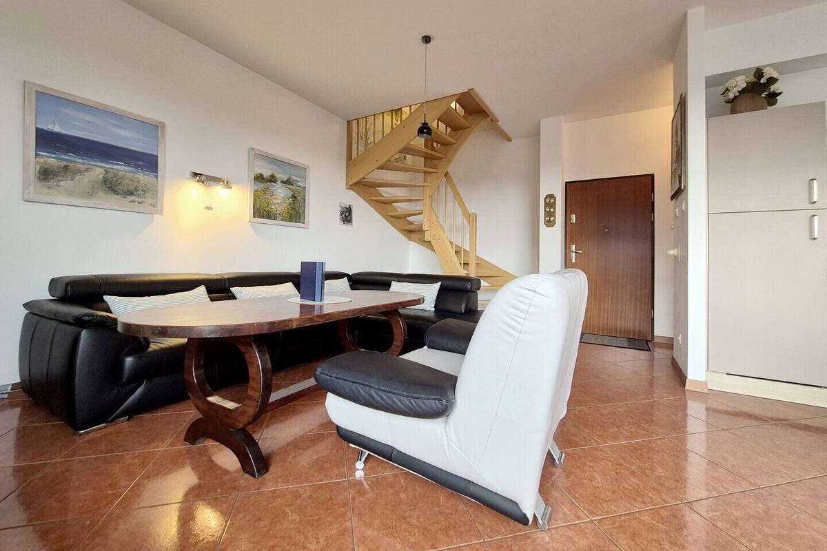 A living room with a black leather sofa, a wooden coffee table, a white armchair, a wooden staircase, and a white cabinet.