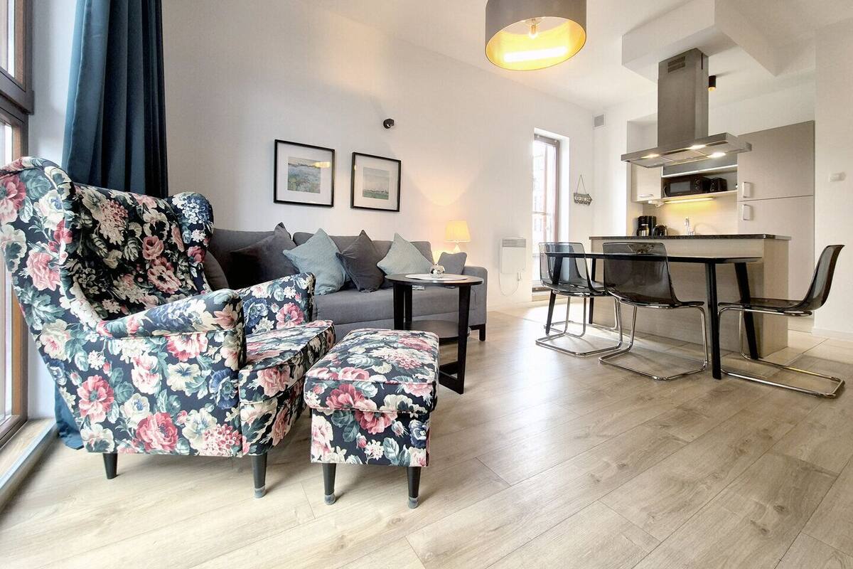 A modern living room with a sofa, floral armchairs, a coffee table, and a dining area with chairs and a table.