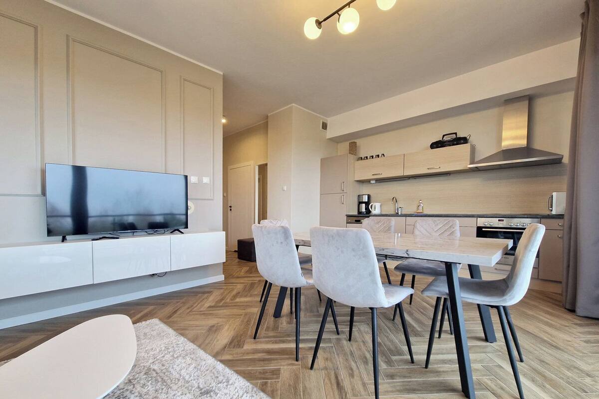 A modern kitchen with a dining area, a TV, and a flat-screen TV on a white cabinet.