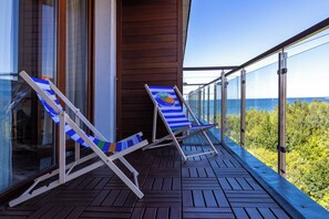 Un balcón con dos sillones de descanso y barandilla de vidrio con vistas a una zona boscosa.