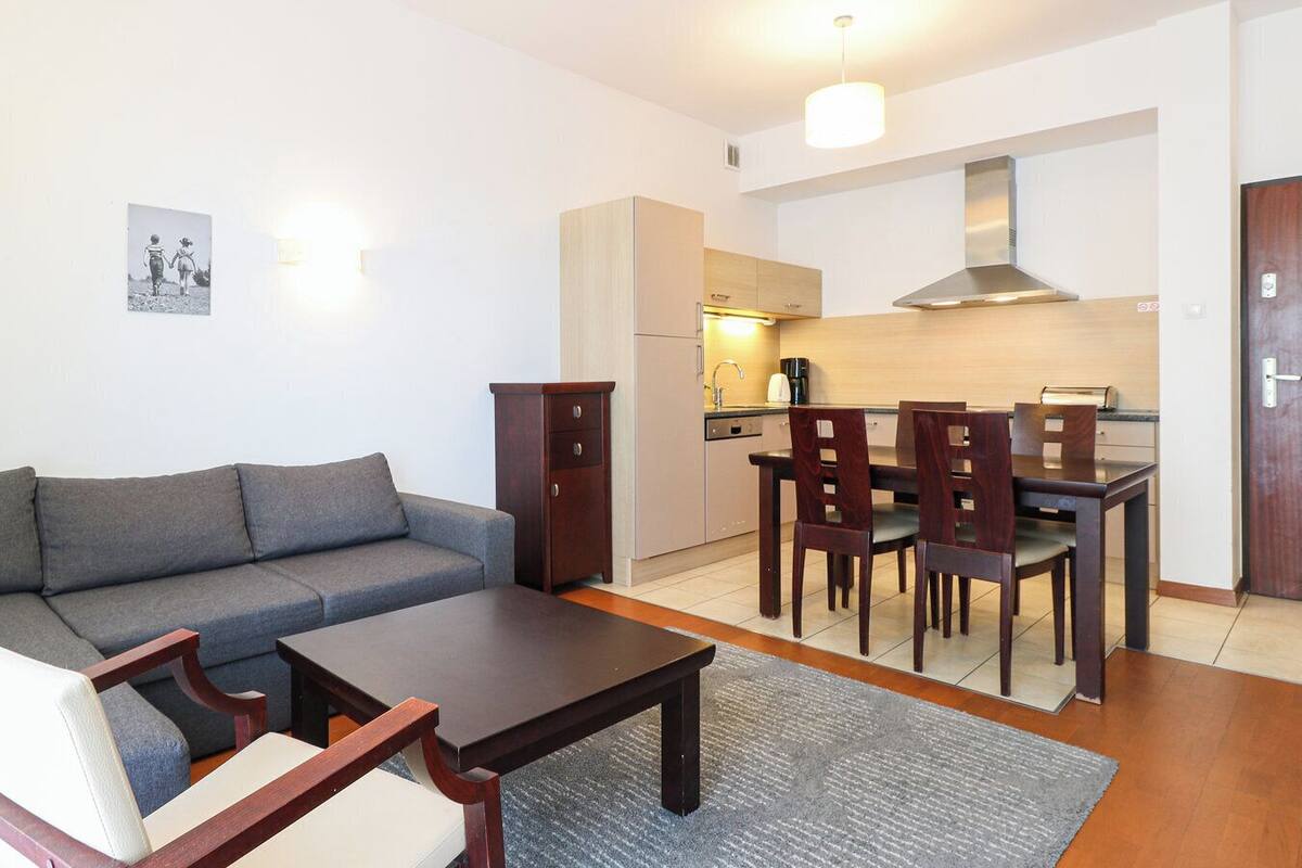 A compact living space with a sofa, a dining table with chairs, a kitchen area, and a small cabinet.