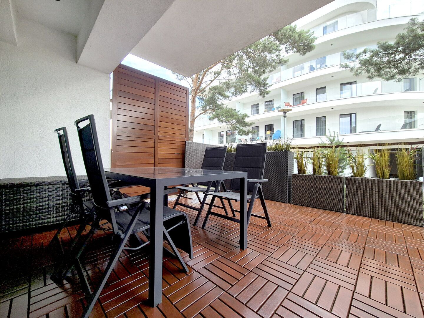 An outdoor patio with a table and chairs, a wooden partition, and a view of a multi-story building.