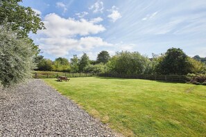 A grassy outdoor area with a gravel path, wooden fence, and picnic table. - Host & Stay | Heather Cottage (Hutton-le-Hole)