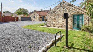 Un bâtiment en pierre avec une porte verte, une allée gravillonnée et une clôture en bois.