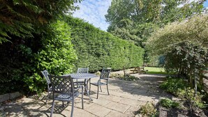 Une terrasse avec une table et des chaises, entourée d’une végétation luxuriante et d’un arbuste taillé avec soin.