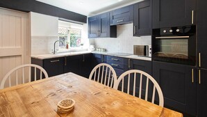 Une cuisine moderne avec des meubles de rangement aux couleurs sombres, une table à manger en bois et des chaises blanches.
