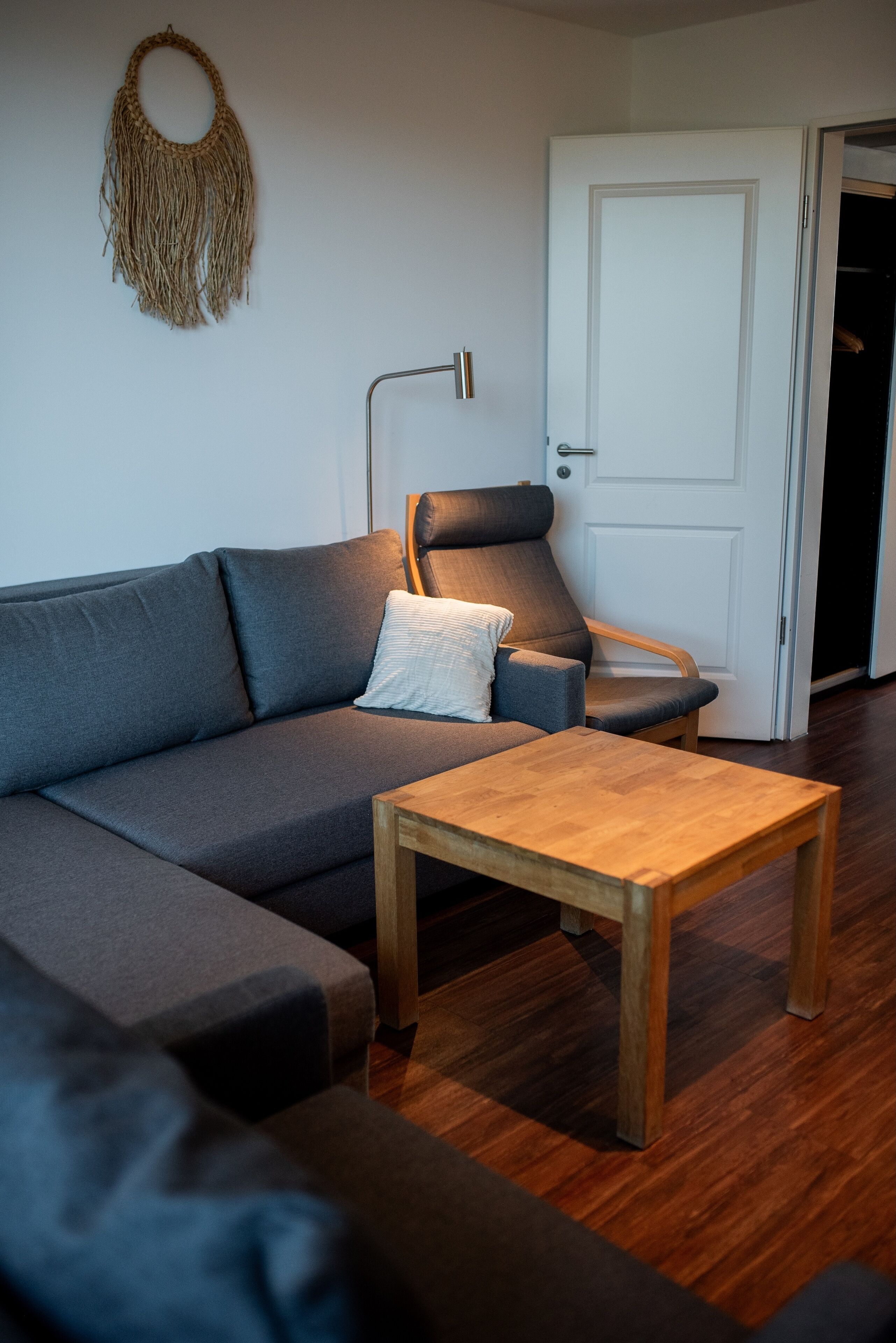 Un salón moderno con un sofá gris, una mesa de centro de madera, un sillón gris y una lámpara de pie.