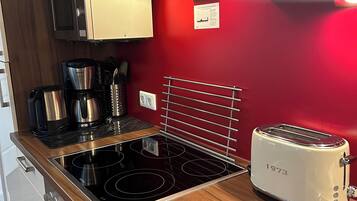 A compact kitchen with a black induction cooktop, a white toaster, and a red wall.