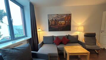 A modern living room with a grey sofa set, a wooden coffee table, and a cityscape painting on the wall.