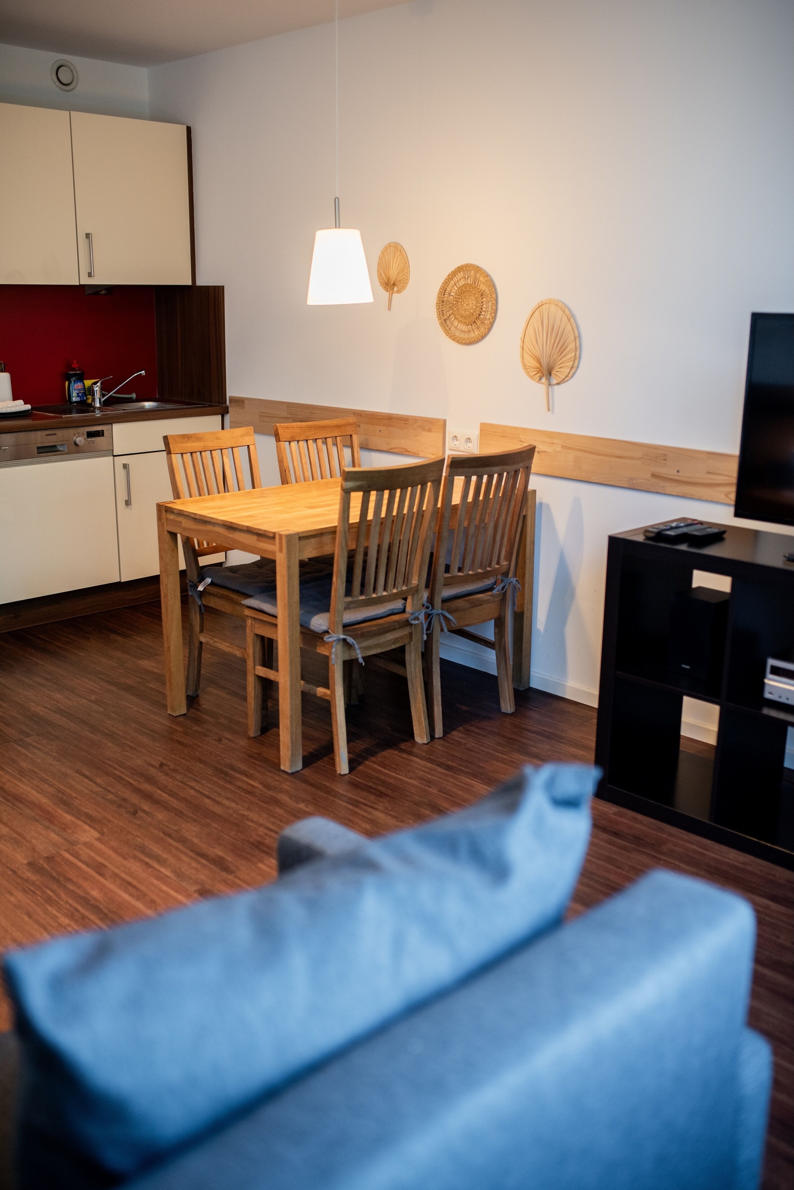 Een moderne keuken met houten kasten, een eettafel met stoelen, en een televisie op een zwarte standaard.