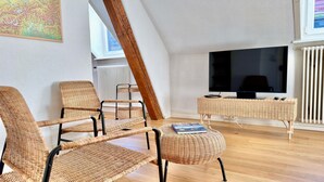 Ein gemütliches Wohnzimmer mit Korbmöbeln, einem Flachbildfernseher und einem großen Fenster.
