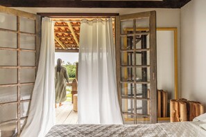 Quarto com cama, uma janela grande com cortinas, teto de madeira e vista para o exterior.
