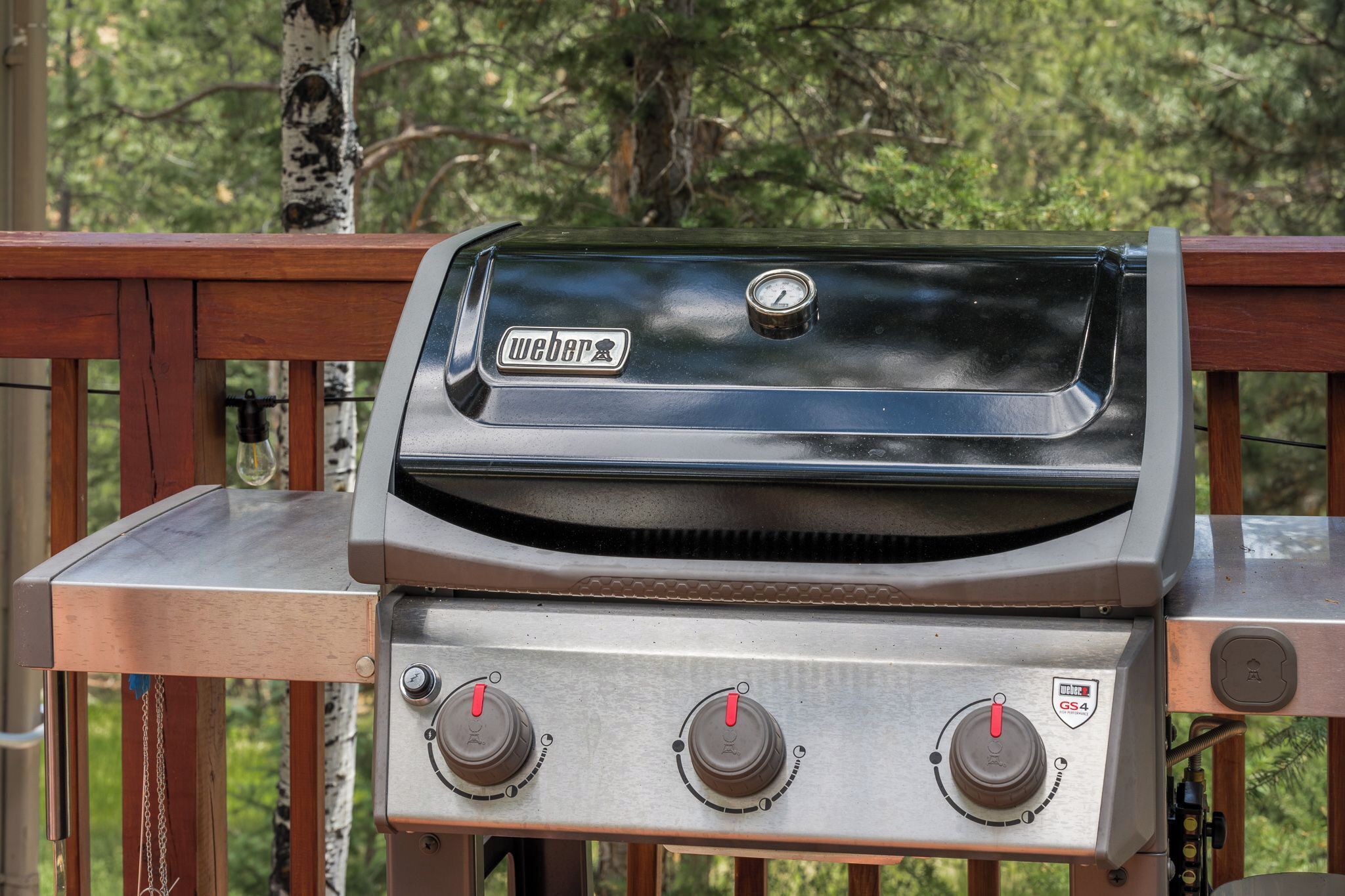 En Weber GS4 gasgrill med tre kontrolknapper og en digital thermometer, monteret på en træterrasse med gelænder af metal.