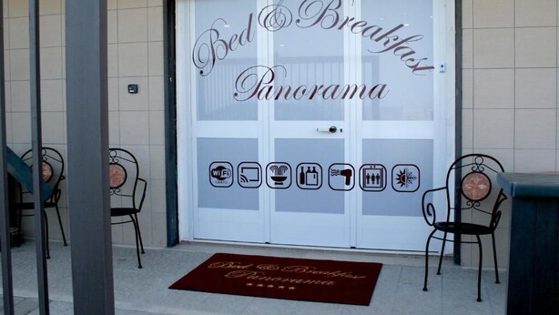 Ein Hotel Eingang mit einem Schild mit der Aufschrift 'Bed & Breakfast Panorama' und Icons, die Annehmlichkeiten wie WLAN, eine Dusche und einen Pool anzeigen.