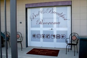 Entrada de hotel con un cartel que dice "Bed & Breakfast Panorama" e iconos que indican servicios como Wi-Fi, ducha y piscina.