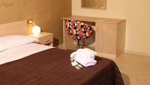 Ein Hotelzimmer mit einem Bett, einem Nachttisch mit Lampe, einem Holzschrank und einem farbenfrohen Stuhl.