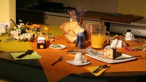 Ein Frühstückstisch ist reichhaltig gedeckt mit verschiedenen Leckereien, darunter ein Krug Orangensaft, ein Glas Milch, ein Teller mit Speisen und ein kleines Kuchenstück.