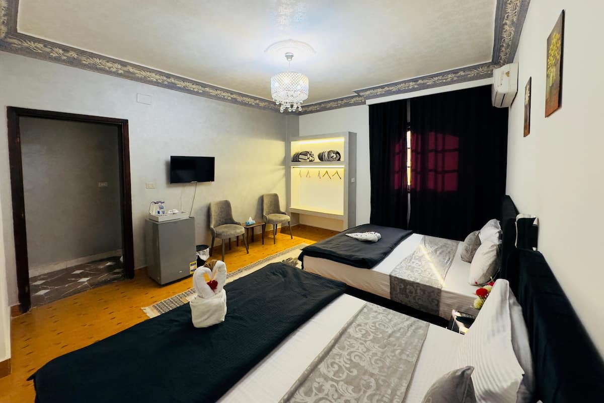 A hotel room with two beds, a TV, a small desk, a chair, and a vanity with a mirror.