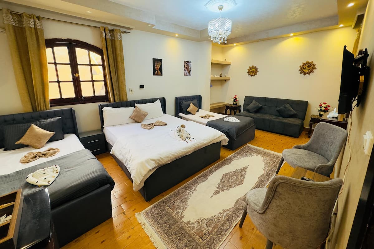 A well-lit bedroom with two beds, a sofa, a chair, and a TV.