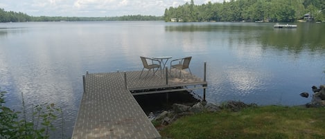 A dock with two chairs and a table, overlooking a calm lake with a forested shoreline.