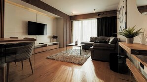 A modern living room with a wooden floor, a flat-screen TV mounted on the wall, a grey sofa, a coffee table, and a dining area with a glass table and chairs. - Nest Inn Magic Apartment Scala Center (Cluj-Napoca)