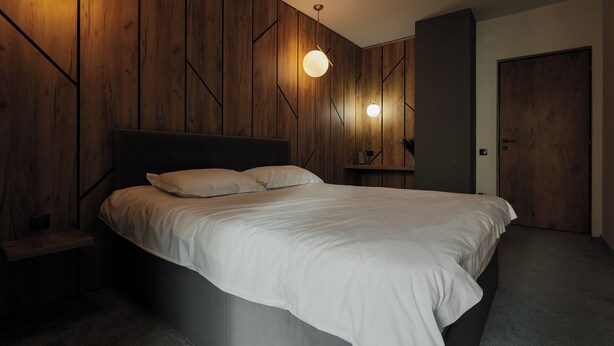 A modern bedroom with a large bed, wooden panel walls, and two wall-mounted lights. - Nest Inn Magic Apartment Scala Center (Cluj-Napoca)