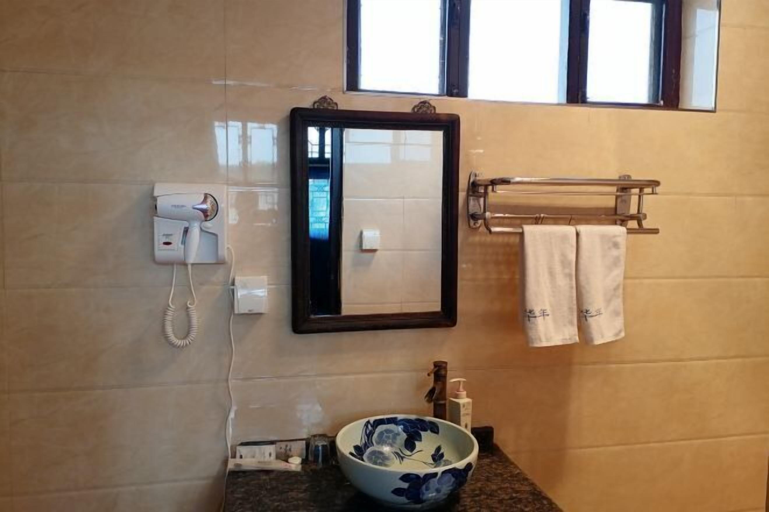 A bathroom with a mirror, a towel rack with towels, a bowl, and a phone.