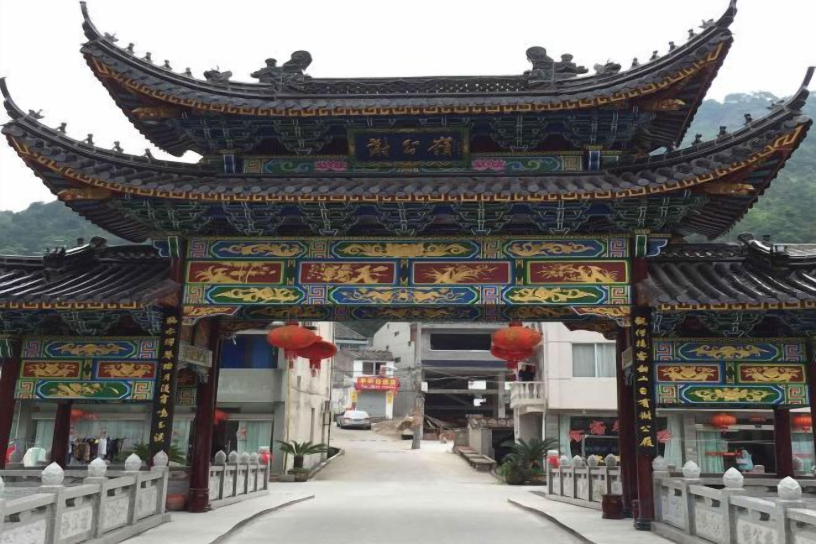 A traditional Chinese gate with intricate designs and characters, leading to a pathway.