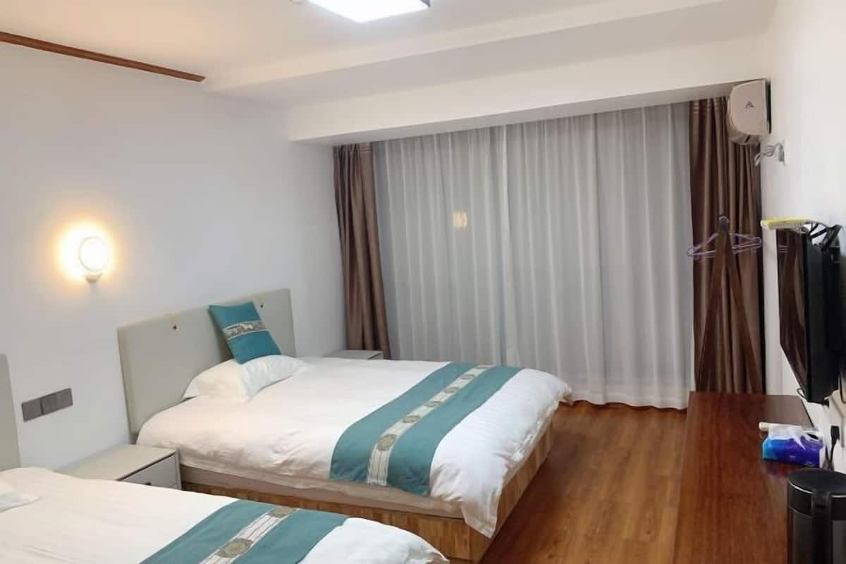 A hotel room with two beds, a wooden floor, a TV, and a window with curtains.