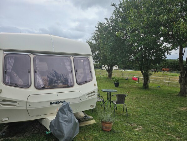 A white camper van parked in a grassy area with a table and chairs nearby.