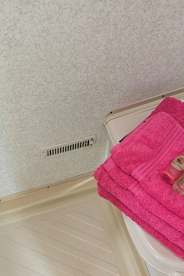 Un baño con piso color beige, inodoro blanco y una toalla rosa a la derecha.