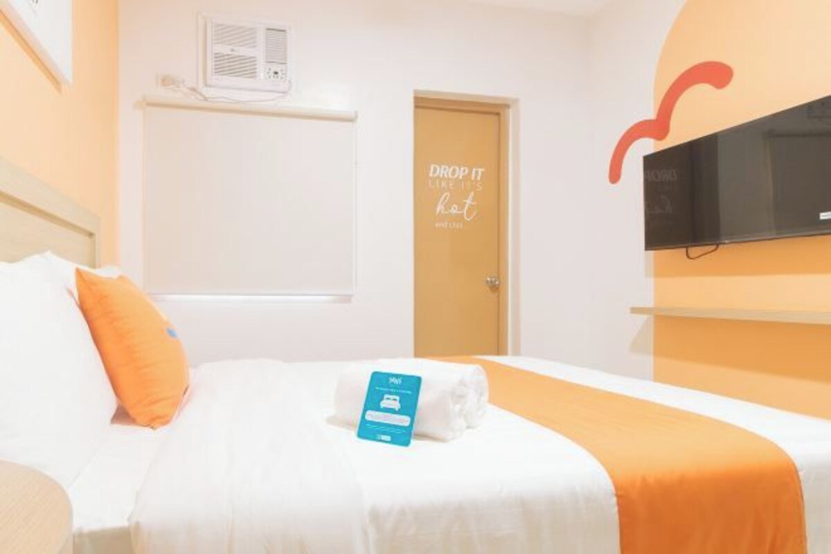 Habitación de hotel con cama, televisor montado en la pared, puerta con una cita motivadora y una toalla sobre la cama.