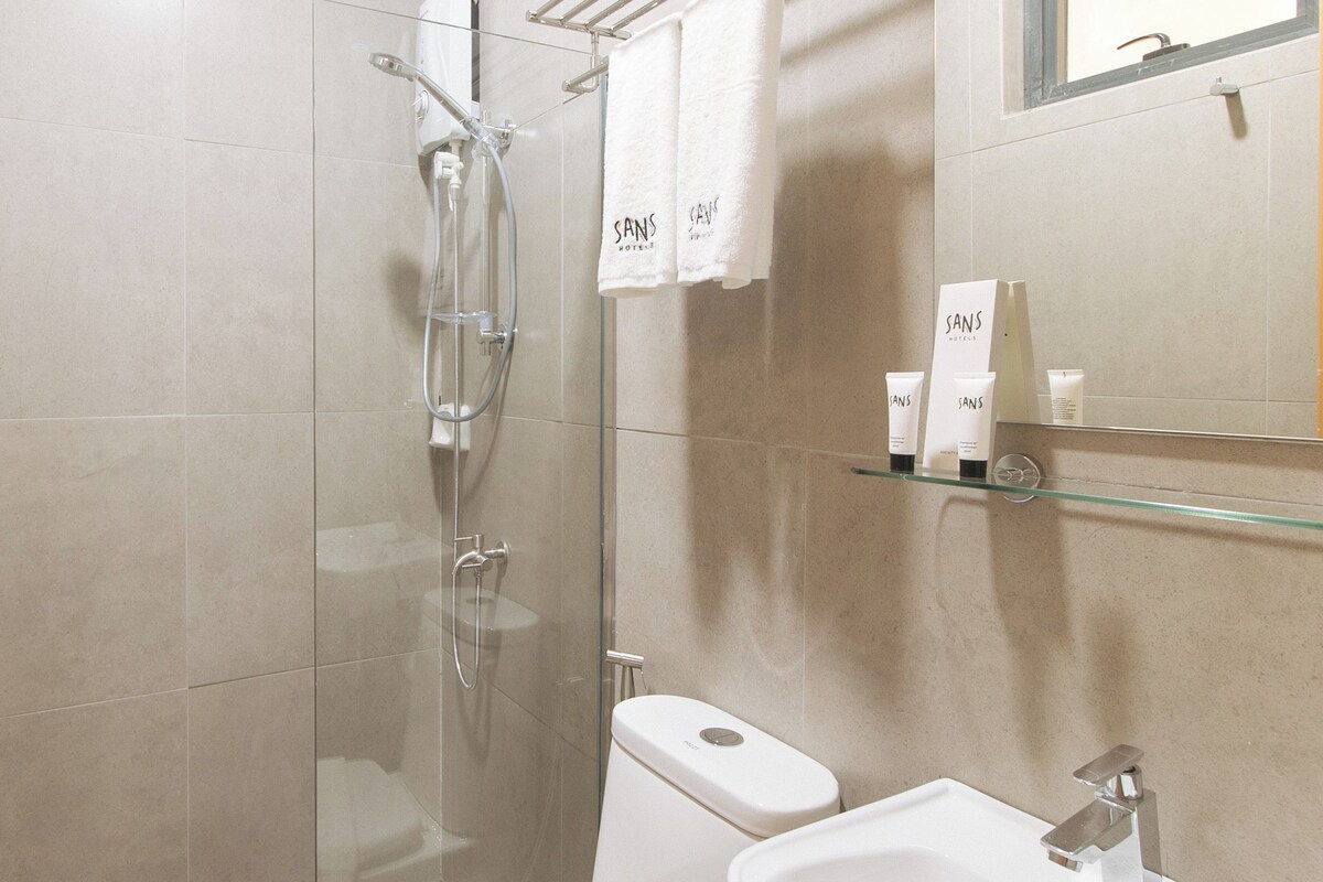 A modern bathroom with a glass-enclosed shower, a toilet, and a sink. There are toiletries on the wall and a towel hanging on a rack.