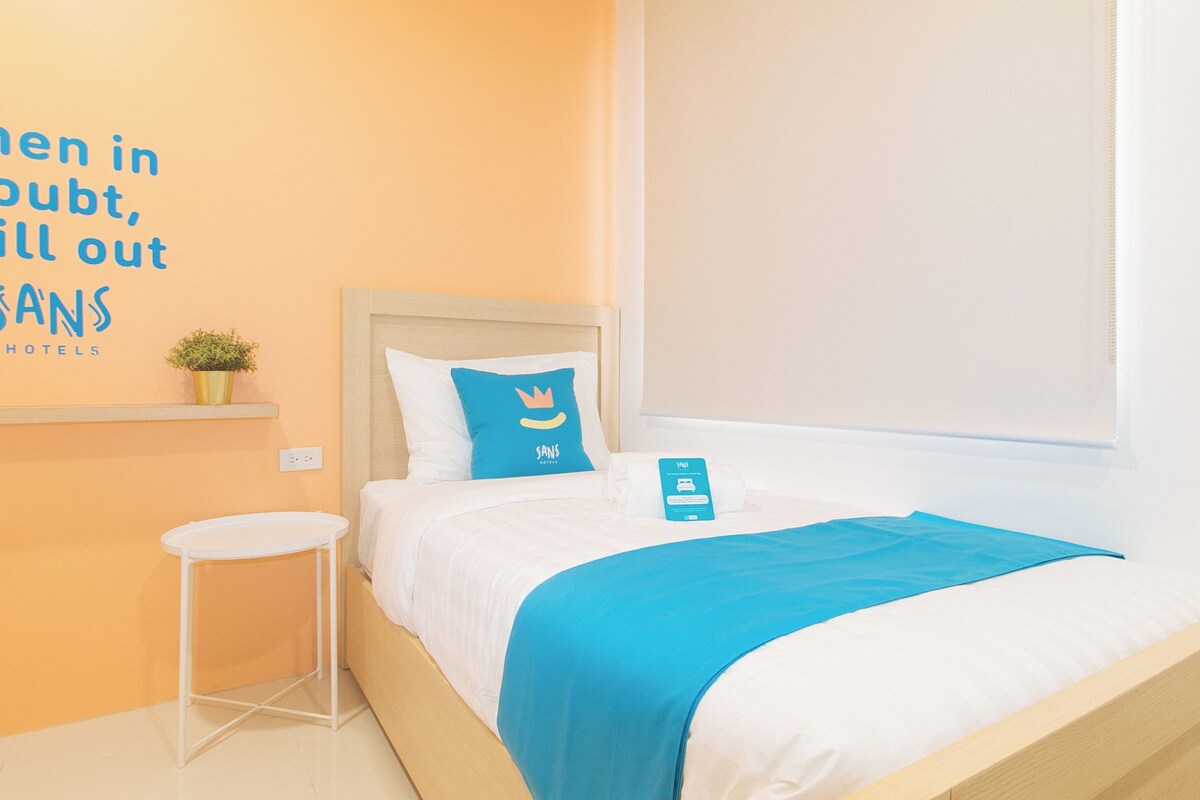Une chambre d’hôtel avec un lit, une petite table, un mur orné d’une enseigne et une fenêtre.
