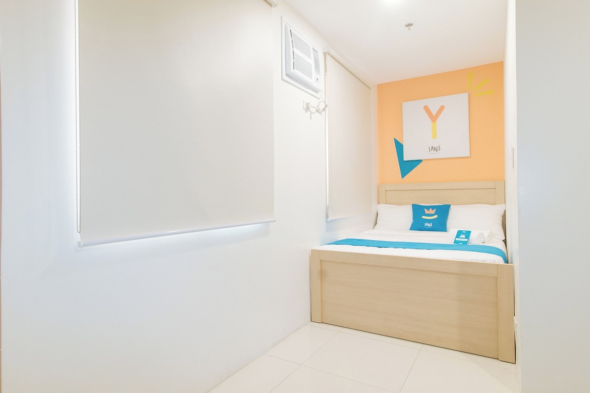 Une petite chambre à coucher moderne, avec un lit, une table de chevet et une étagère fixée au mur.