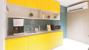 Una cocina con gabinetes amarillos, un lavamanos, una cafetera, un microondas y una pequeña planta en maceta sobre la encimera.