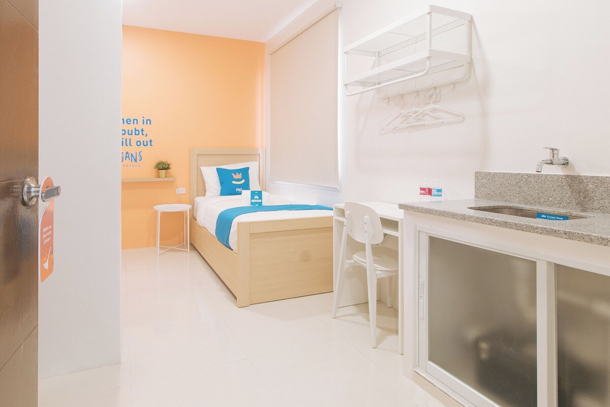 Habitación de hotel con cama, una mesita, una silla, un lavabo y un espejo.