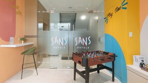 Un hall de hotel con una mesa de fútbol de mesa, un mostrador de recepción y una entrada con puerta de vidrio.