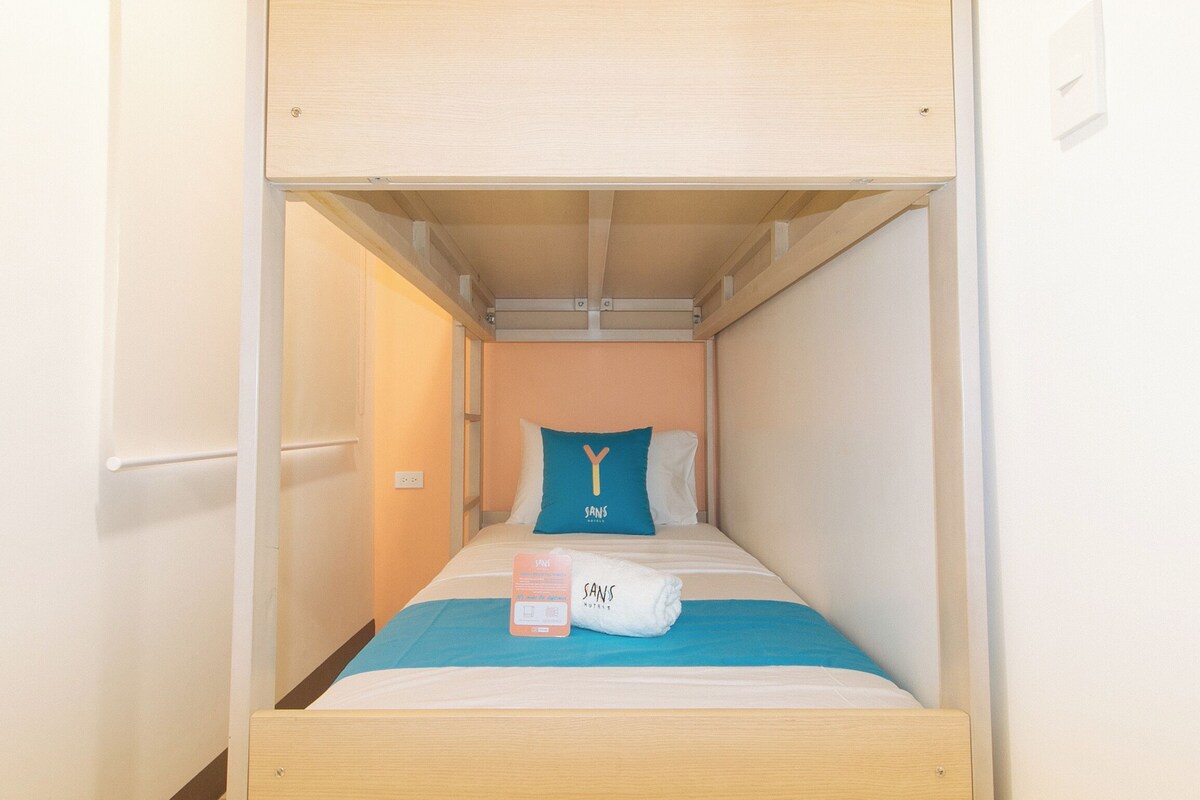 Una habitación pequeña con una cama individual, cabecera de madera, almohada azul, almohada blanca y una toalla sobre la cama.