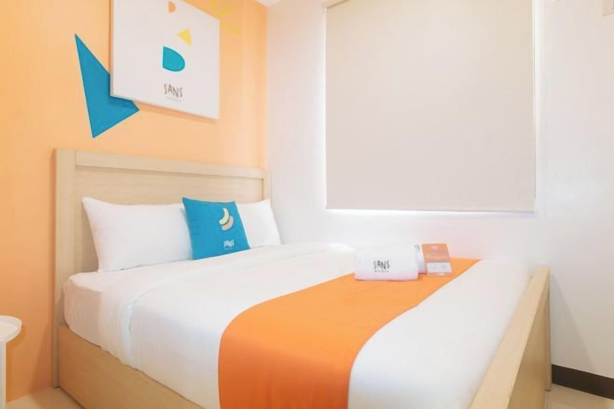 A hotel room with a bed, a nightstand, and a window with a blind.