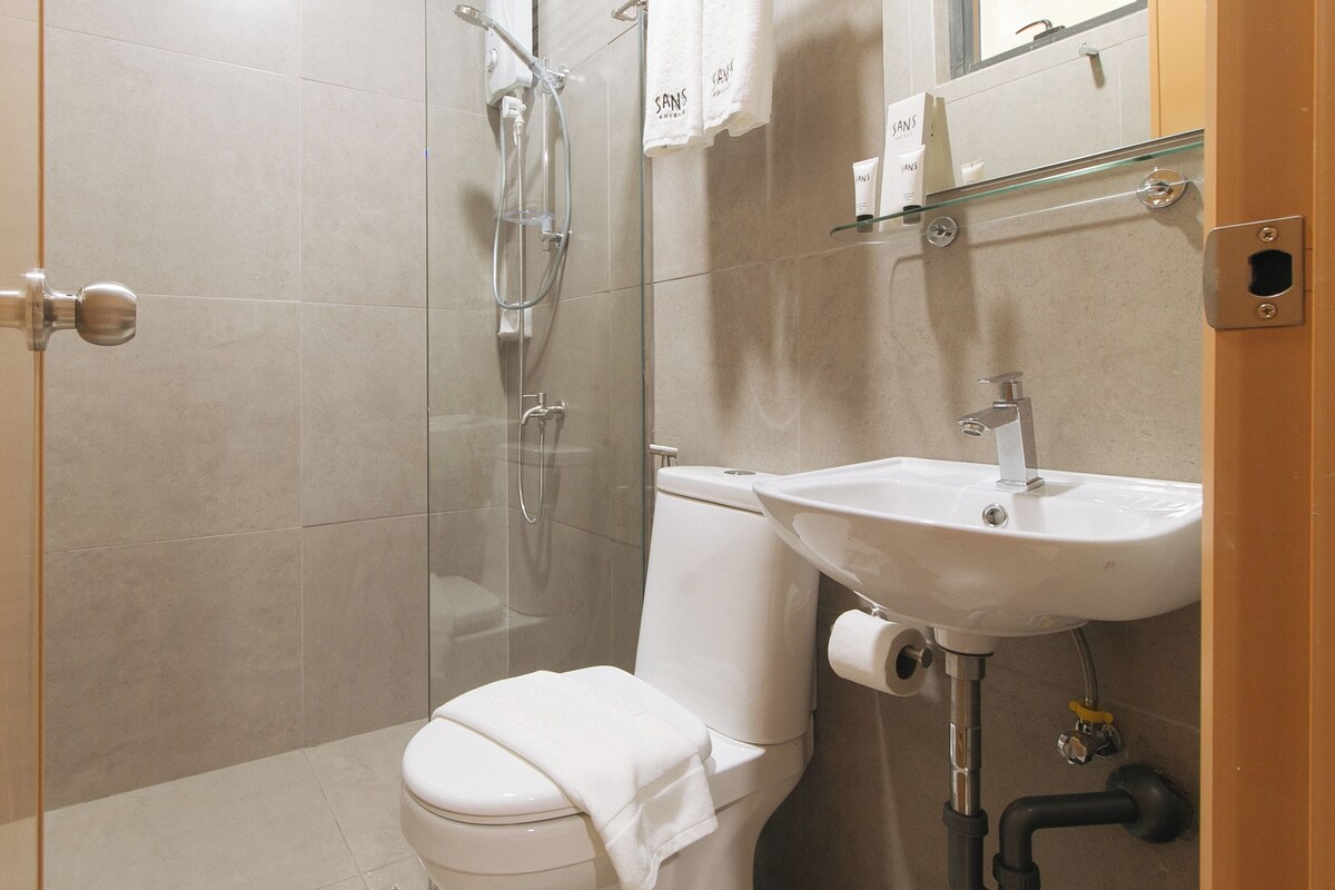 Une salle de bain moderne avec une douche à parois de verre, des toilettes blanches et un lavabo surmonté d’un miroir.