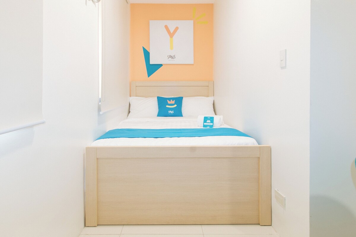 Una cama bien hecha con una colcha azul y almohadas, un cabecero de madera y un letrero en la pared con la letra 'Y' y la palabra 'sans'.