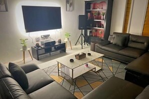 A modern living room with a flat-screen TV, a sofa, a coffee table, and a bookshelf.