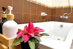 A bathroom with a bathtub, a wooden side table, a potted plant, and two bottles of liquid soap.
