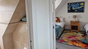 A bedroom with a bed, a nightstand, a lamp, a teddy bear, a colorful rug, and a painting on the wall. - Highland House in Ullapool (Ullapool)