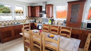 A kitchen with wooden cabinets, a dining table with chairs, and a microwave. - Highland House in Ullapool (Ullapool)