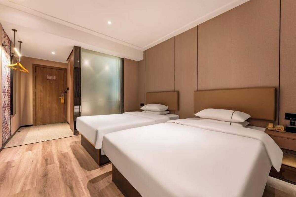 Ein Hotelzimmer mit zwei Betten, einer Holztür, einer Wandleuchte und einem kleinen Tisch mit einem Telefon.