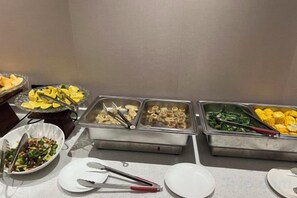 Un buffet proposant divers plats présentés dans des récipients en métal, notamment des pâtes, des légumes et du maïs.