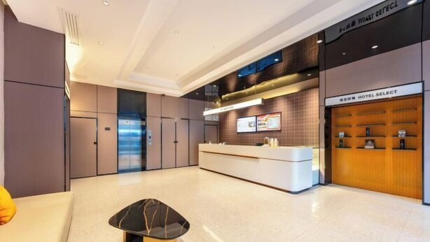 A modern hotel lobby with a reception desk, a seating area, and a wall-mounted display. - Bai Man Hotel (Guangzhou Financial City Tangxia Metro Station) (Guangzhou)
